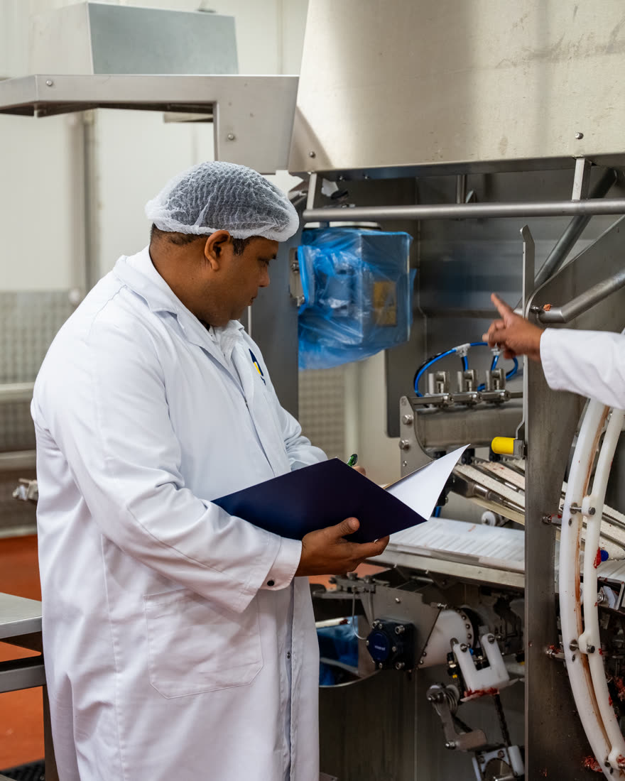 Emera supervisor in lab coat and hairnet recording a machine inspection on a clipboard