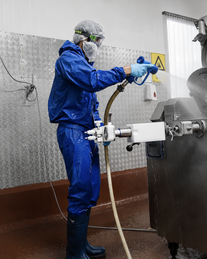 Emera technician in full protective coveralls pressure-cleaning processing machinery