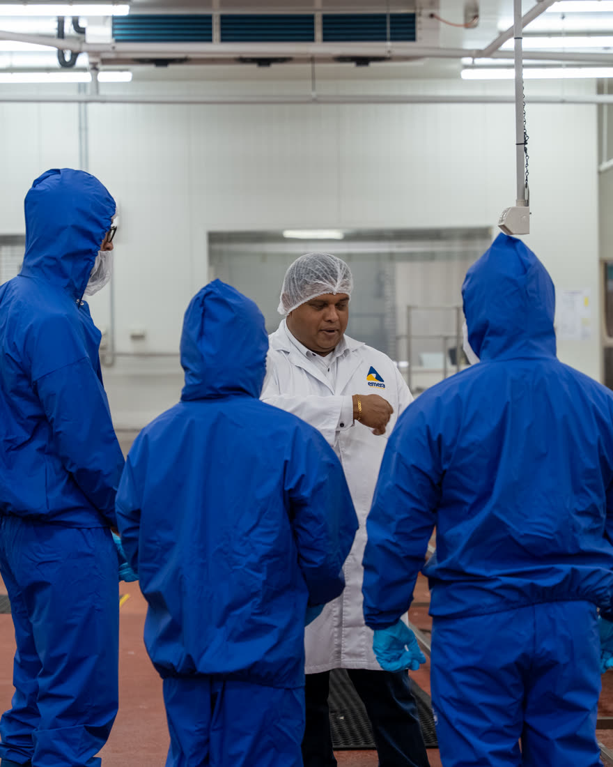 Emera supervisor briefing a cleaning crew in full protective coveralls inside a food plant